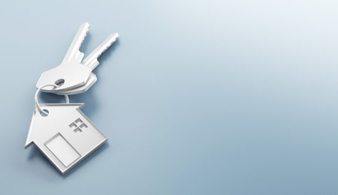 White house-shaped keychain on a light blue gradient background, symbolizing home ownership