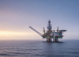 Ceny ropy klesajú po Trumpovom odklade útokov na Irán Offshore oil rig in the calm sea at sunset with a warm orange and purple sky behind it.
