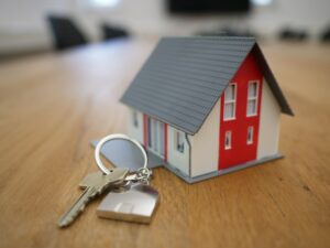 Hypoteka Miniature house model with a set of keys on a wooden table, representing home ownership or real estate knowledge.
