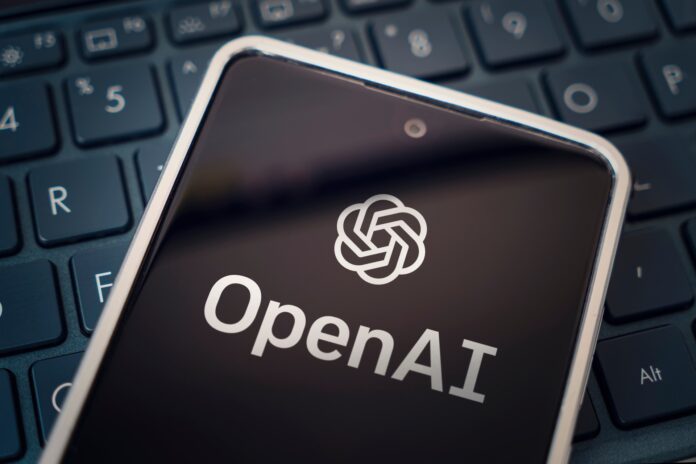 Close-up of a smartphone on a keyboard showing the OpenAI logo on the screen.