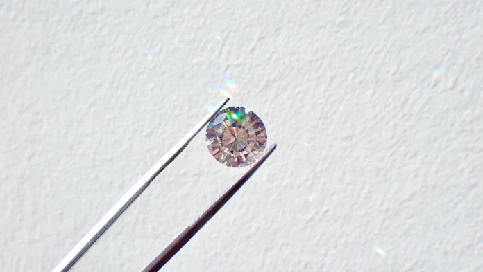 Round-cut diamond held by tweezers against a light textured background, center-focused